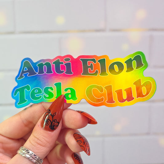 Colorful cutout text 'Anti Elon Tesla Club' held by a hand with painted nails against a light background.