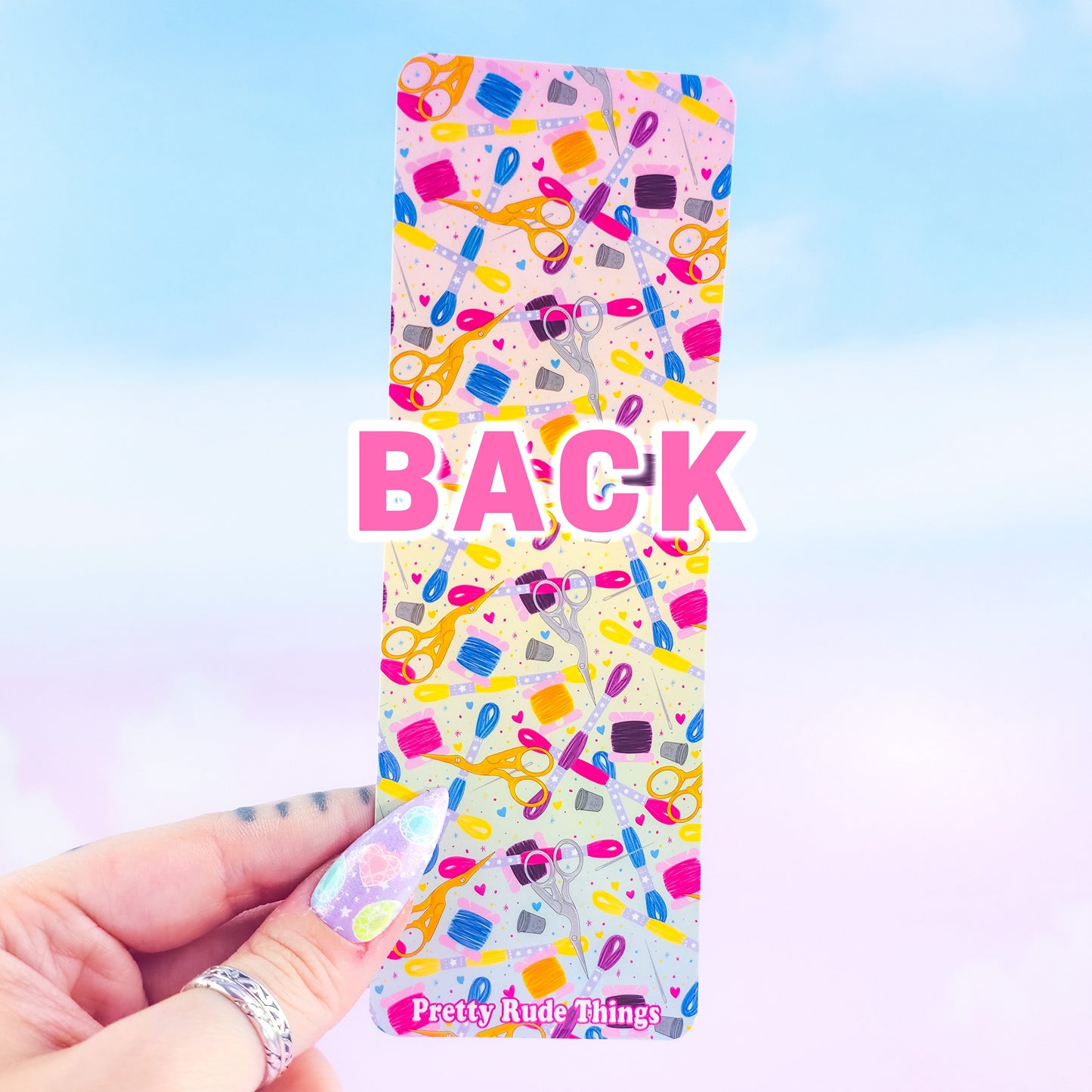 Back of embroidery holographic bookmark – colorful sewing supplies pattern with scissors, floss, and thimbles, handmade by Pretty Rude Things