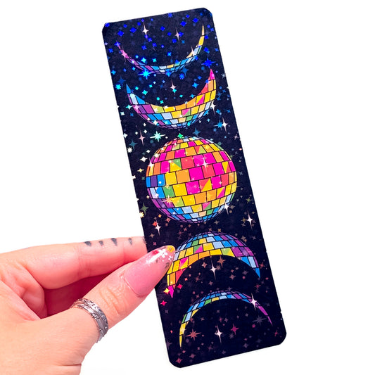A hand holding a slim rectangular card featuring a cosmic disco theme with a mirrored disco ball, crescent moons, and stars on a dark background.