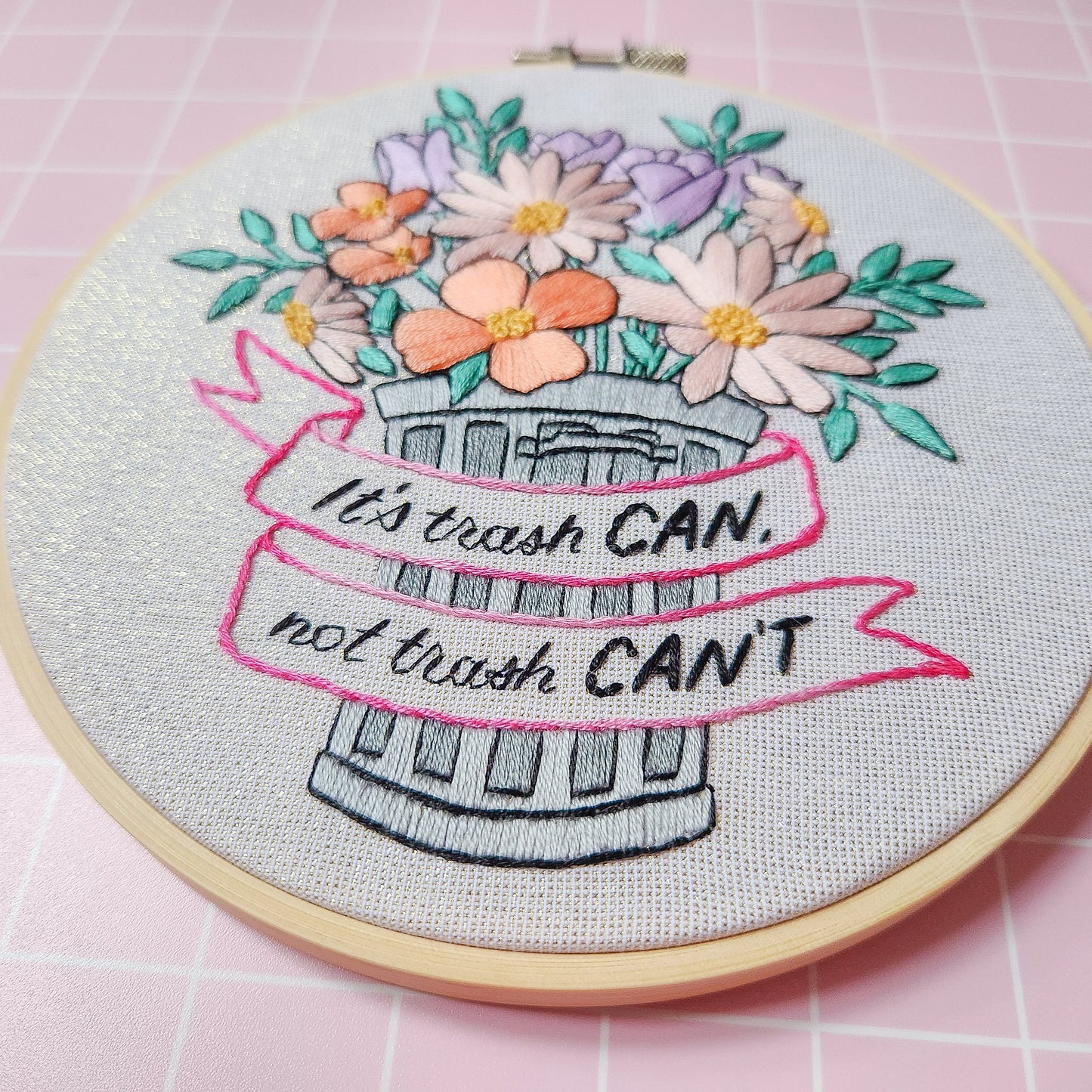 An embroidery piece with a trash can with flowers in it saying "it's trash can not trash Can't"