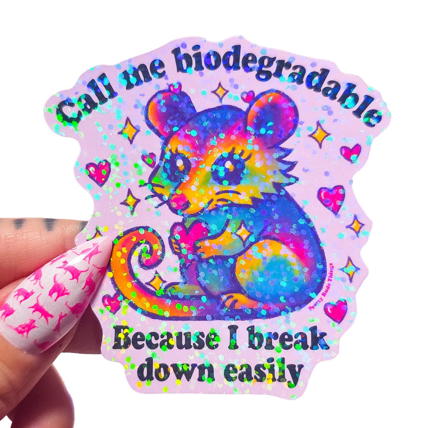 Colorful sticker with a cartoon possum holding a heart and text that says "Call me biodegradable because I break down easily" on a light pink background
