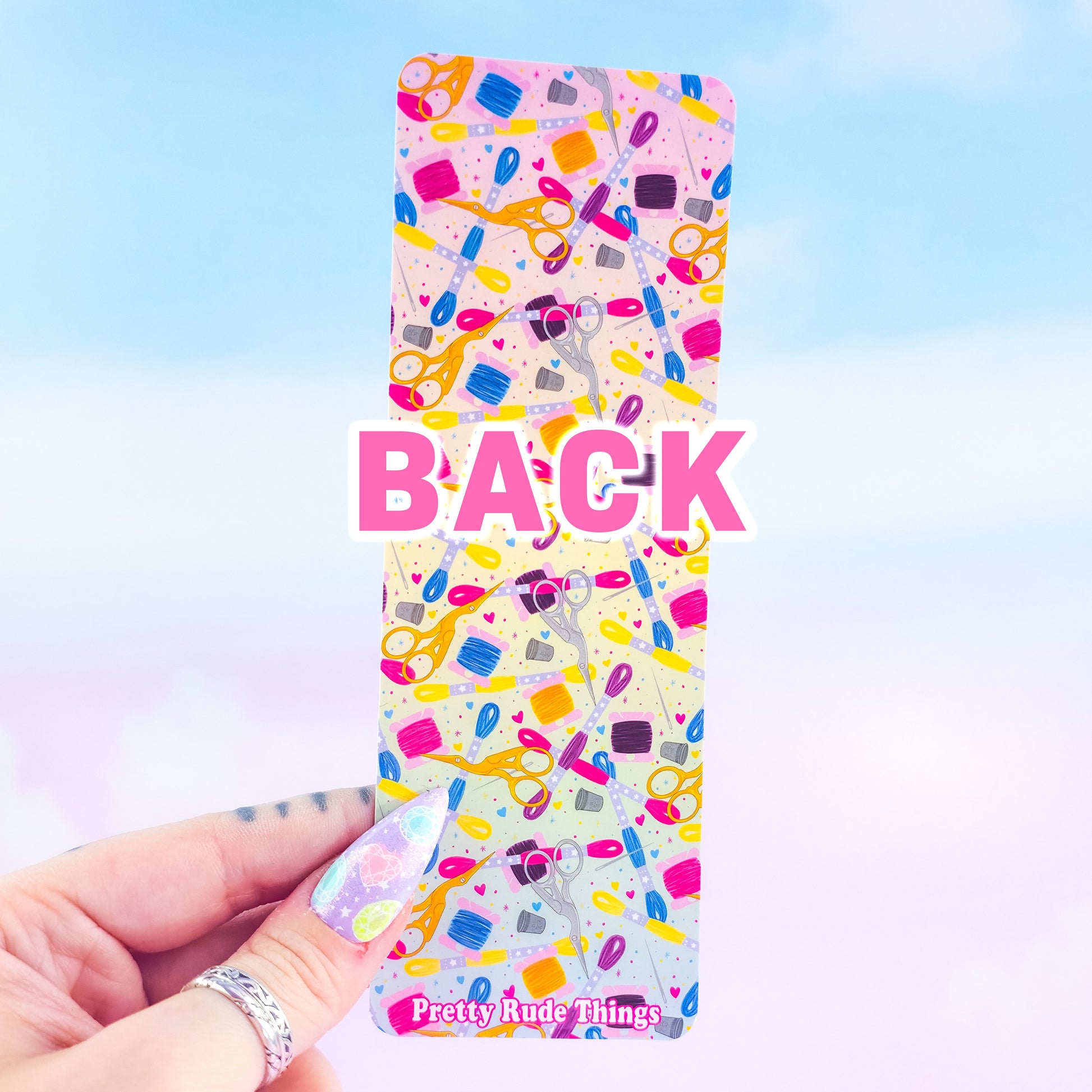 Back of embroidery holographic bookmark – colorful sewing supplies pattern with scissors, floss, and thimbles, handmade by Pretty Rude Things