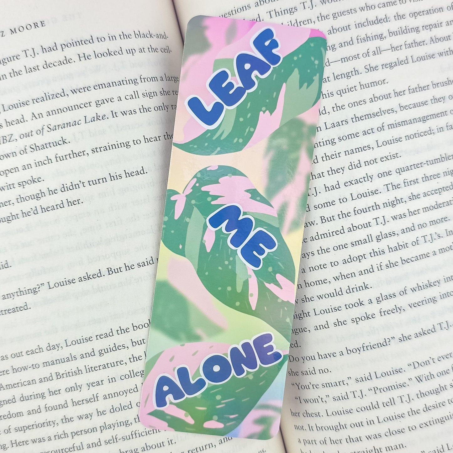 Leaf Me Alone holographic bookmark with pink princess philodendron leaves placed inside open book – funny pun gift for plant lovers