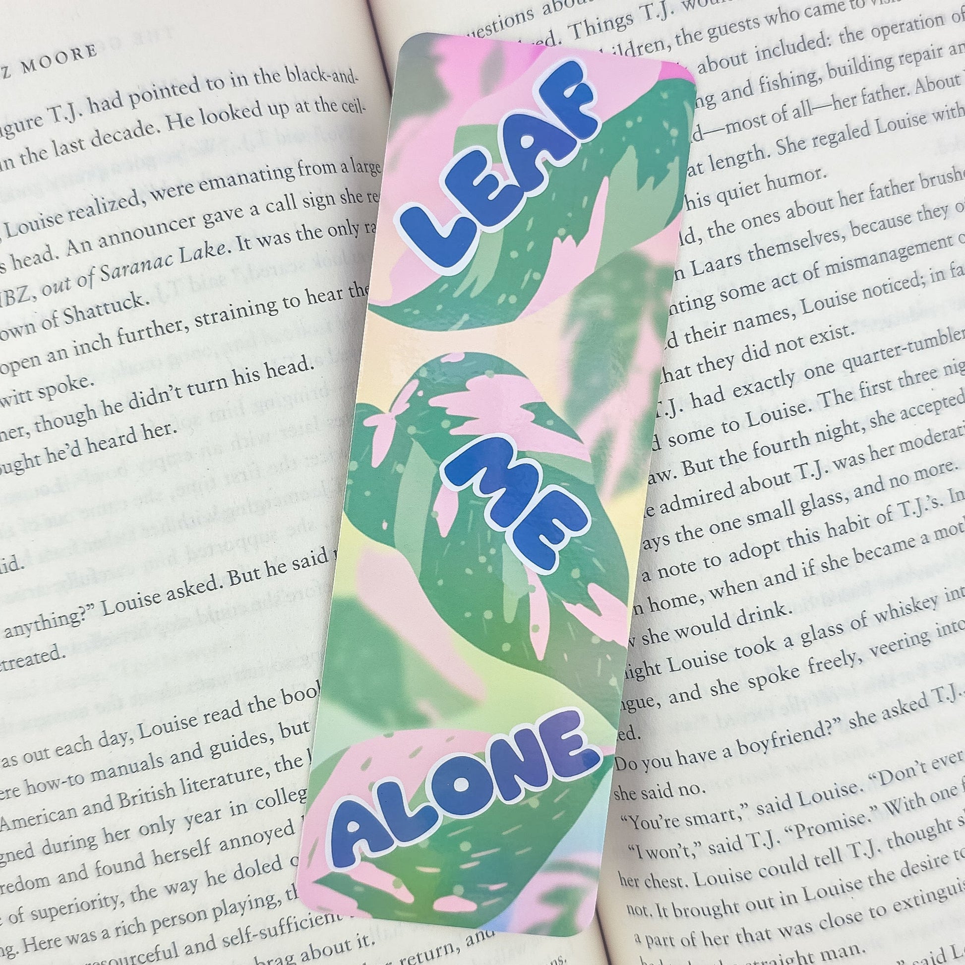 Leaf Me Alone holographic bookmark with pink princess philodendron leaves placed inside open book – funny pun gift for plant lovers
