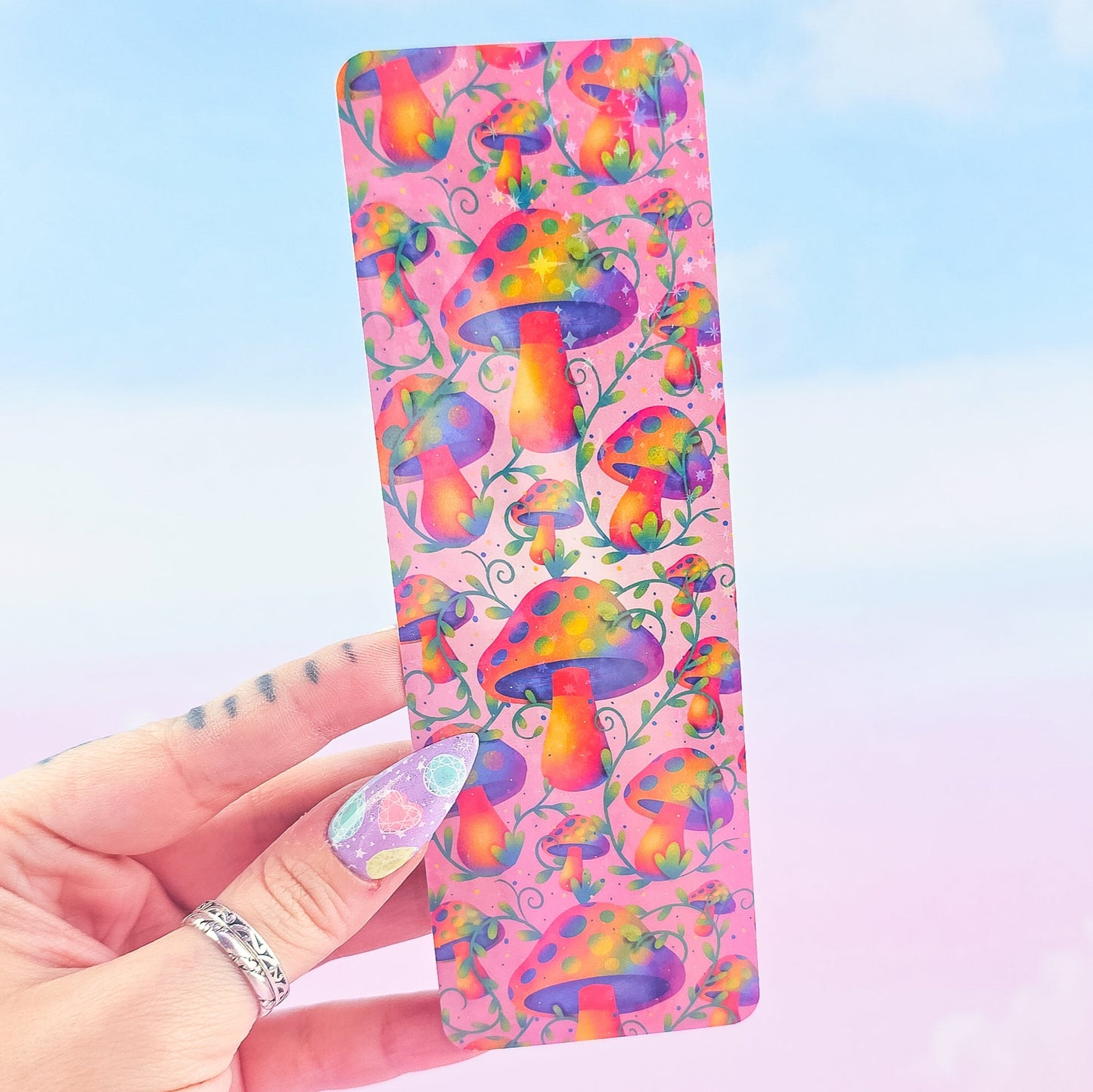 Rainbow mushroom holographic bookmark without tassel, shiny laminated finish, held against sky background