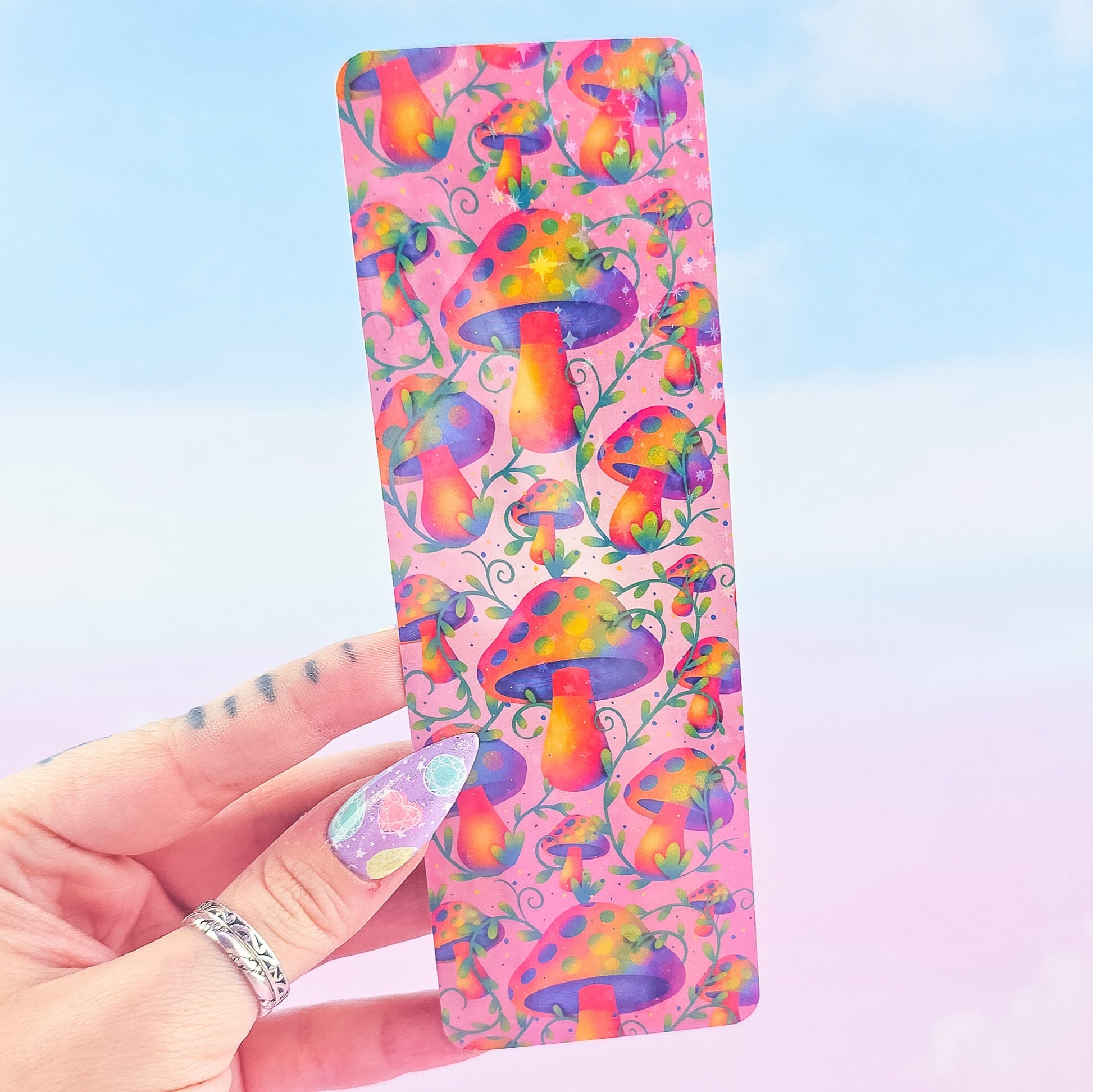 Rainbow mushroom holographic bookmark without tassel, shiny laminated finish, held against sky background