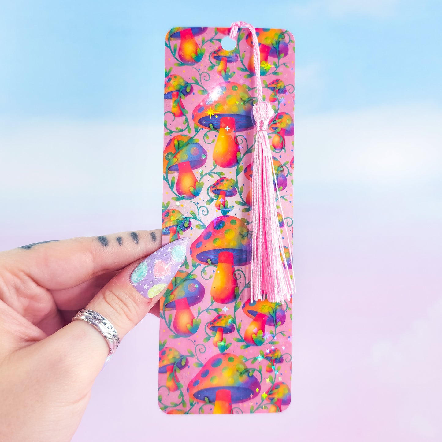 Rainbow mushroom holographic bookmark with pink tassel, handmade and glossy, shown in hand