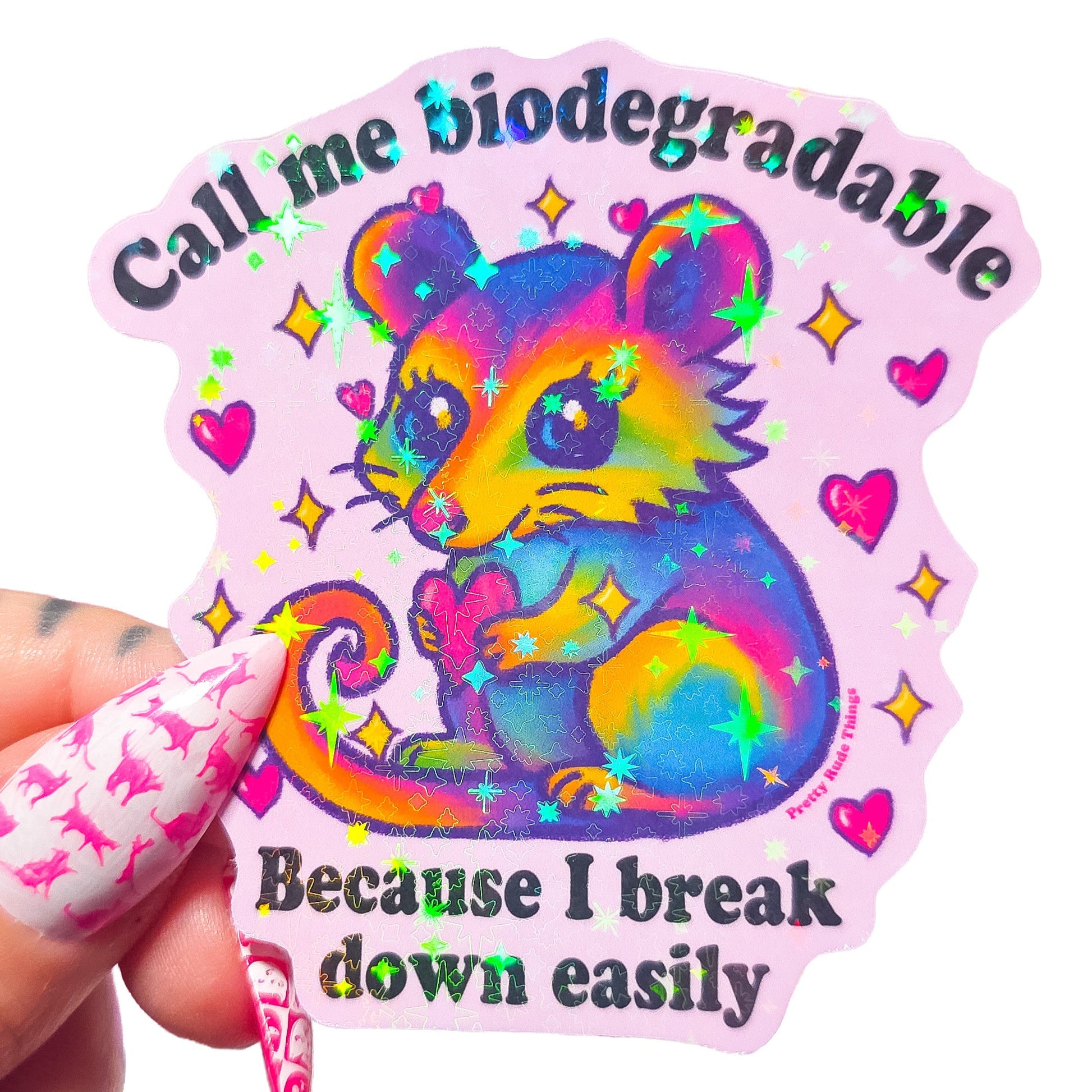 Colorful sticker with a cartoon possum holding a heart and text that says "Call me biodegradable because I break down easily" on a light pink background