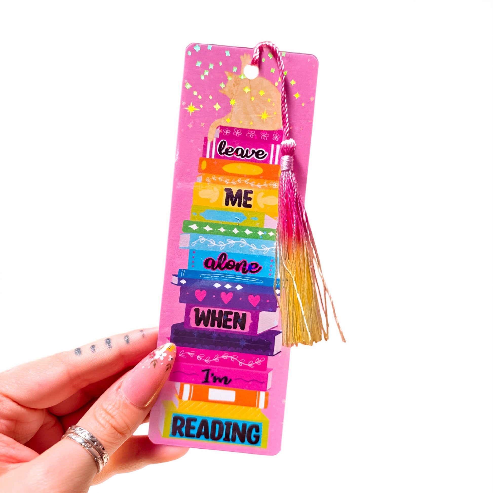 Holographic bookmark with a cat on a stack of books and the words Leave Me Alone When I'm Reading, with tassel, on a white background