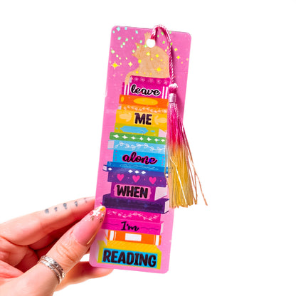 Holographic bookmark with a cat on a stack of books and the words Leave Me Alone When I'm Reading, with tassel, on a white background